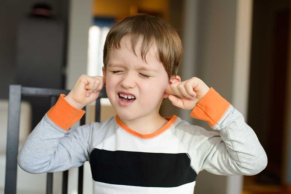 Boy pressing his fingers into both ears with a pained look, a sign of clogged ears, from Better Hearing Rehabilitation Center in Durham, NC